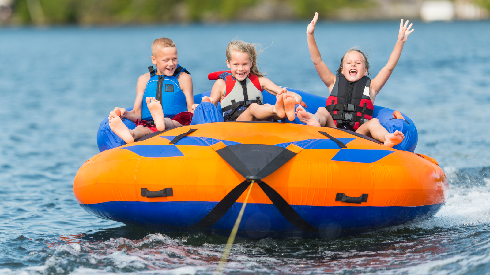 Three laughing children wearing life jackets on inner tube on a body of water